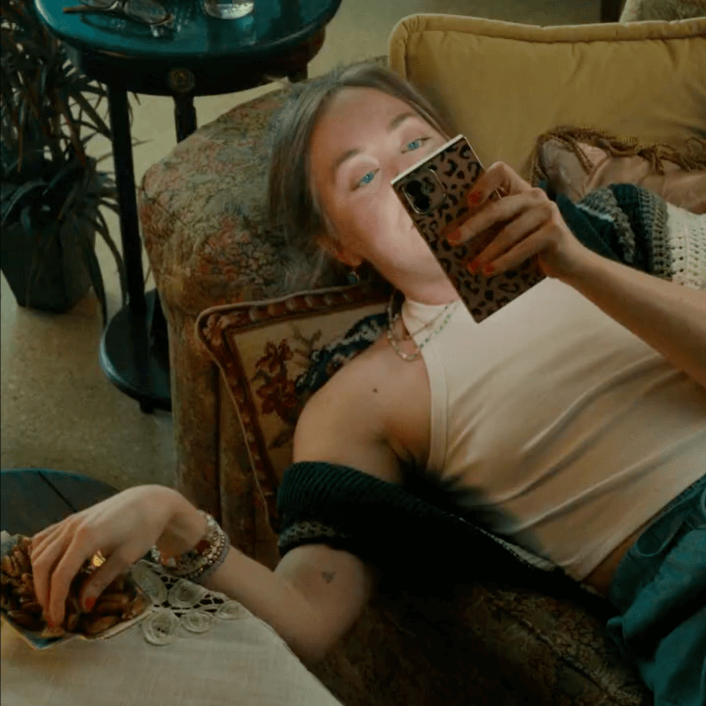 Woman laying on couch looking at phone while snacking on bowl of pecans